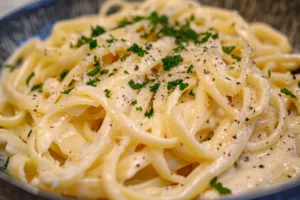 Bowl of homemade creamy Alfredo sauce topped with parsley.